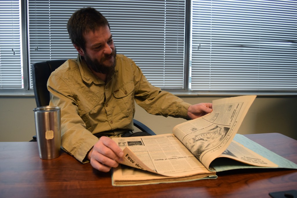 a man flips through a book of newspapers