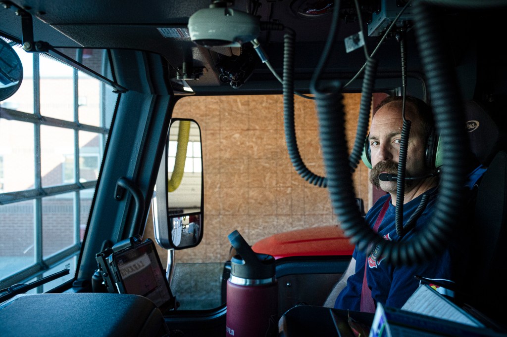 A firefighter sitting in the left seat of a fire engine.