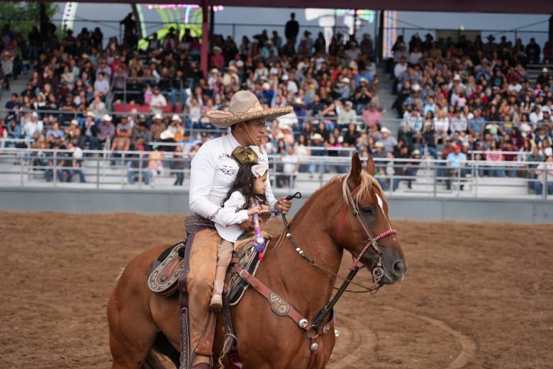 A man holds a child as they ride a horse.