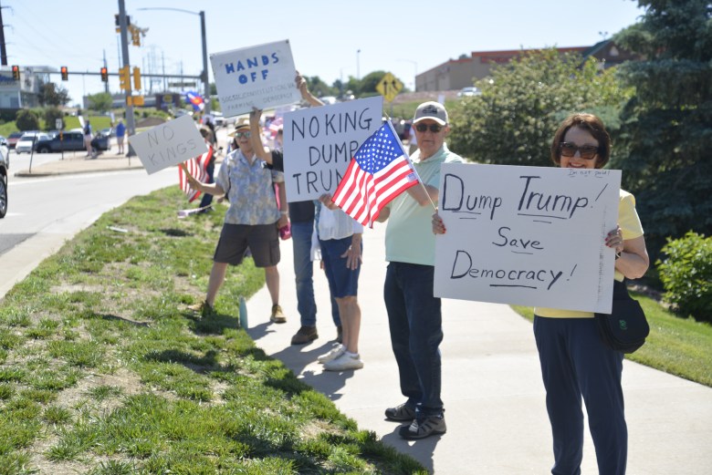 A group of people stand on a sidewalk, holding signs at a protest.