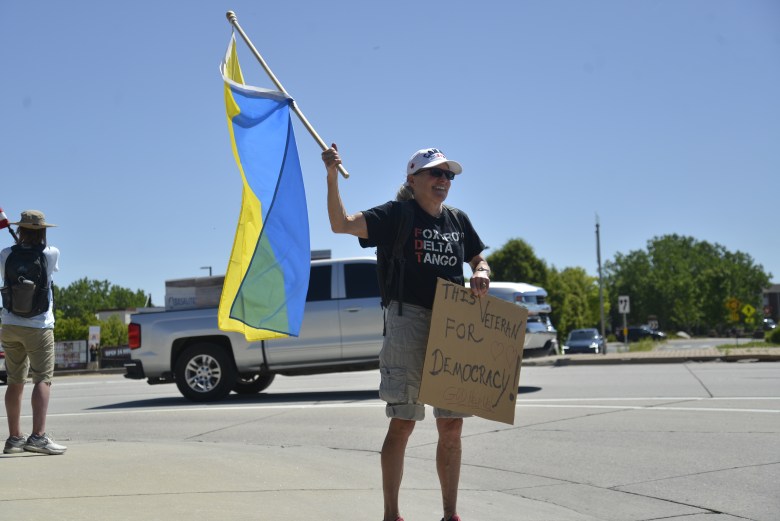 A woman holds a Ukrainian flag on the corner of an intersection.