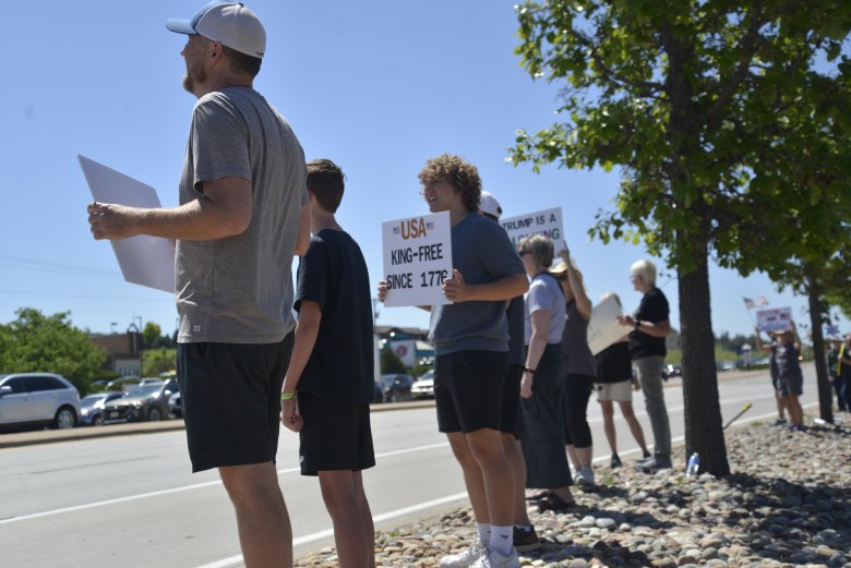 A group of people lined up on the side of the road, holding signs.