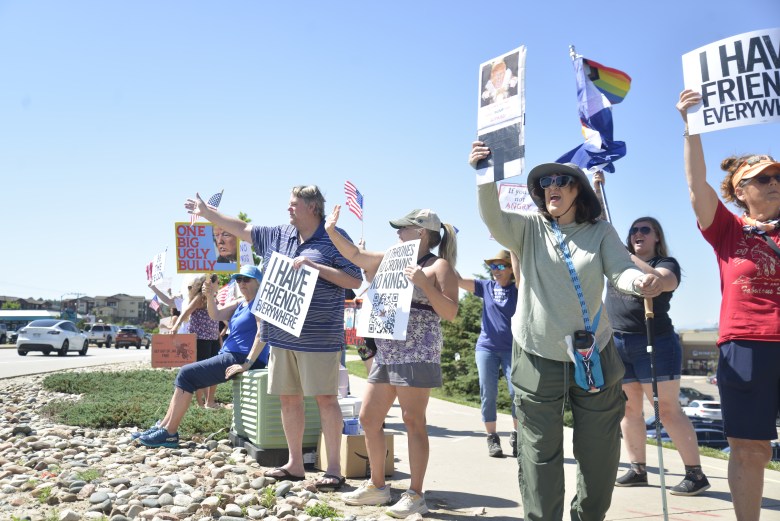 A group of people hold signs and wave to people at the corner of an intersection.