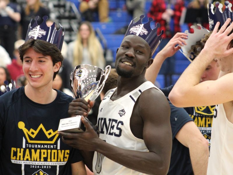 At center, Colorado School of Mines guard Majok Deng holds the 2025 RMAC Tournament trophy as he and his teammates celebrate winning the March 8 championship game against Regis