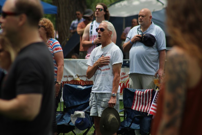 The crowd stands for the national anthem as one attendee, at center, sings along during Golden's 4th of July Festival at Lions Park.