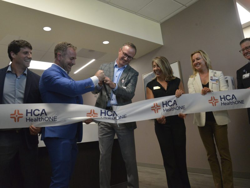 A group of people use large scissors to cut a ribbon at a ceremony.