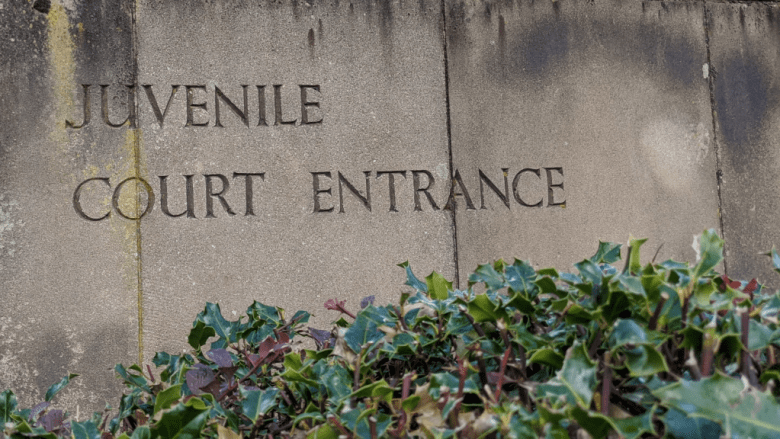 Weathered stone slab sign with the words juvenile Court Entrance engraved into it with foliage at the bottom Outside the Department Of Justice courthouse where juveniles are tried.